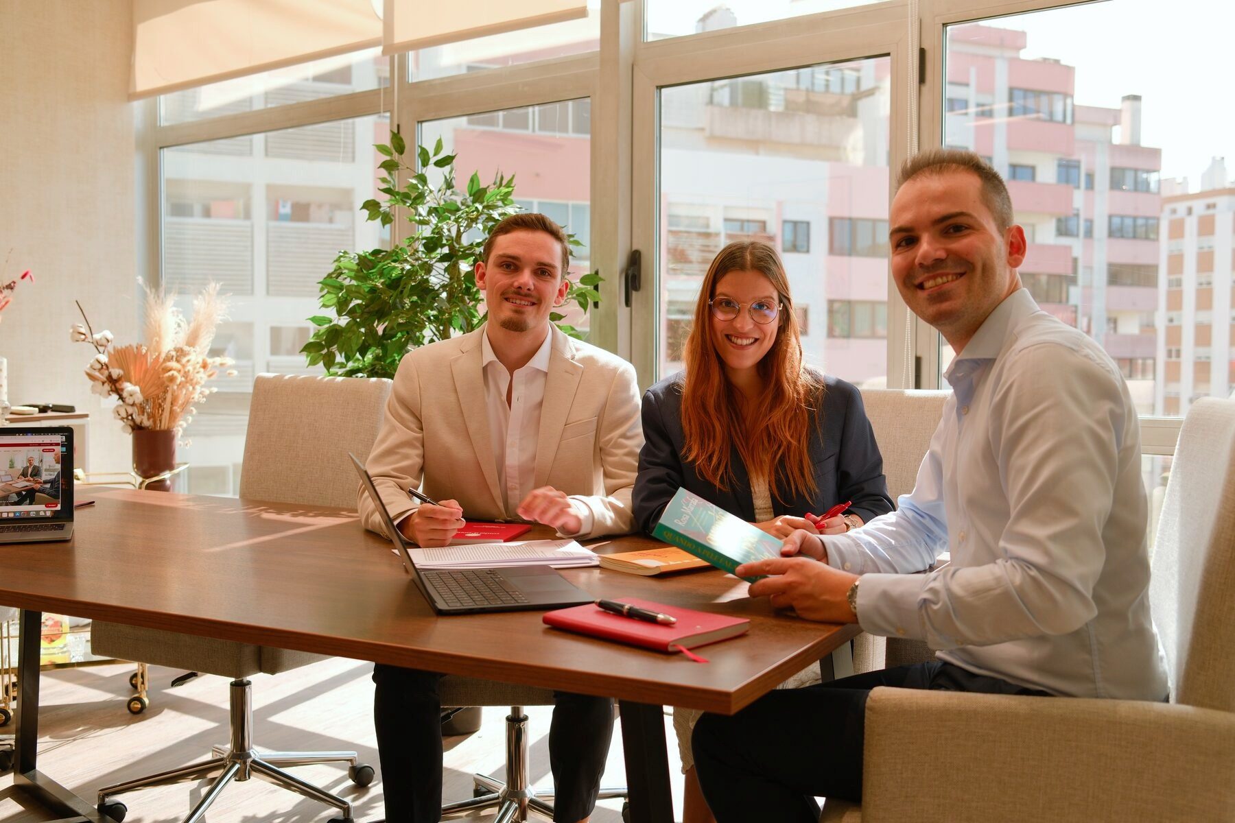 Três elementos da equipa editorial à mesa de reunião, com livros e um original em papel