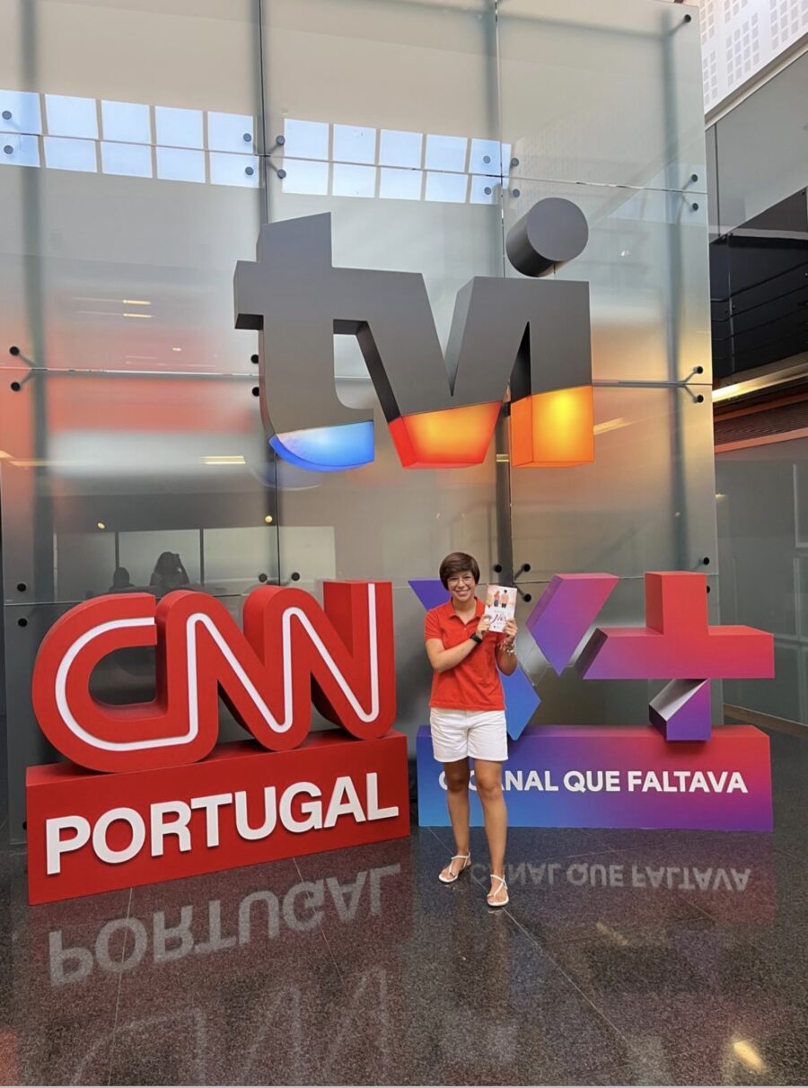 Autora da casa à entrada dos estúdios de televisão, com os letreiros dos canais