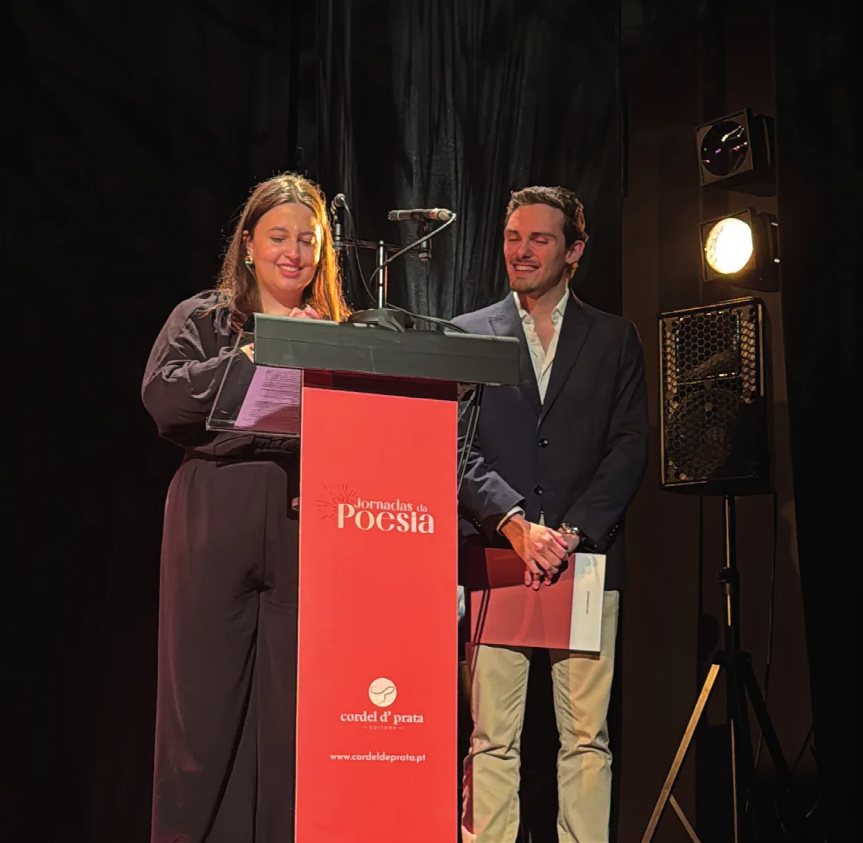 Duas pessoas ao púlpito das Jornadas da Poesia, uma delas a ler